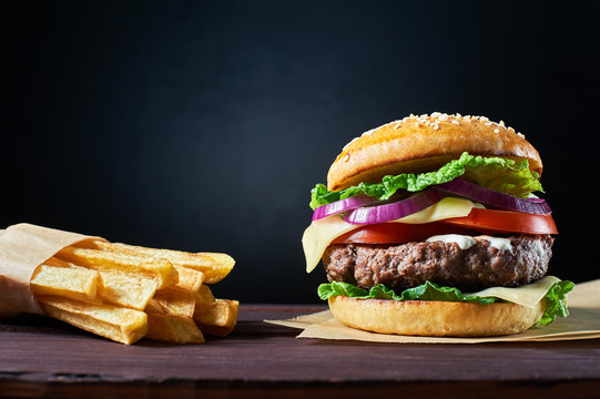 Craft beef burger and french fries on wooden table isolated on dark blue background.