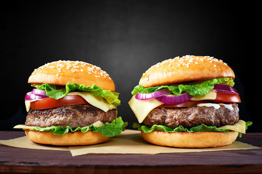 Two craft beef burgers on wooden table isolated on black  background.