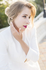 Beautiful blonde girl with red lips in a business white trouser suit, with hair styling and professional makeup on a sunset background. The concept of successful and strong woman close up portrait