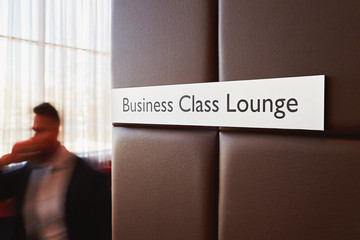 Metal door sign Business Class Lounge on leather bound wall in modern airport with unrecognizable...