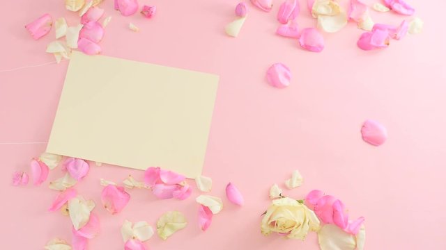 Yellow empty sheet of paper is moving among the rose petals on pink background