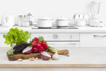 Wooden table with vegetables on top over blurred kitchen interior