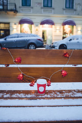 Garland of red Christmas trees hangs over red cup standing on wooden bench