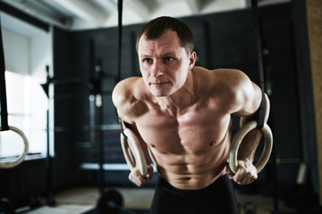 Fototapeta na wymiar Intense crossfit workout in dark gym: mature male bodybuilder performing arm muscle endurance test on rings