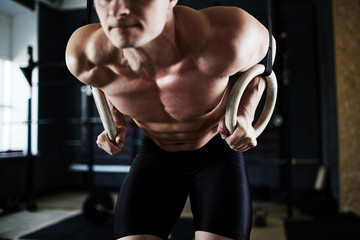Fototapeta na wymiar Intense crossfit workout in dark gym: closeup shot of male torso with bulging tense muscles at work during gymnastic rings exercise