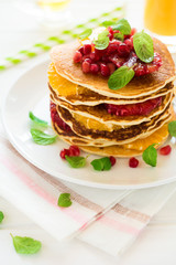 Traditional breakfast: stack of pancakes with orange slices and pomegranate seeds decorated mint leaves on white wooden table. Selective focus