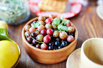 Close-up view of gooseberries and blackcurrant straight out of garden lying in round wooden bowl on table