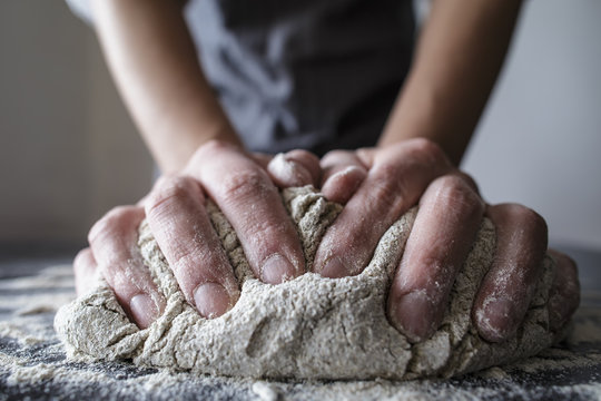 close-up of human hands in the apron knead the dough on a black wooden table, sprinkle with flour