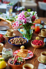 Seasonal table setting with fresh-cut field flowers, gooseberries and raspberries from garden, hot waffles and cups of tea