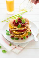 Traditional breakfast: stack of pancakes with orange slices and pomegranate seeds decorated mint leaves on white wooden table. Selective focus