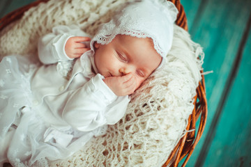 Fototapeta na wymiar Baby-girl dressed in white clothes with laces sleeps in the basket