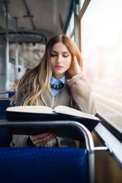 Beautiful young woman sitting in city bus and reading a book. 