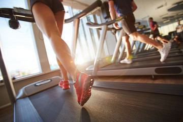 Low-angle view of male and female legs running on treadmill in gym on sunny day