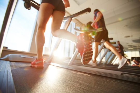 Female athlete in mini shorts warming up on treadmill on beautiful sunny morning