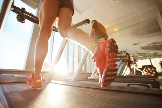 Low-angle view of athletic female legs in mini shorts jogging on gym treadmill