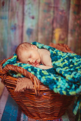 Green and yellow scarf envelopes little baby sleeping on plaid in basket