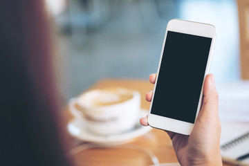 Mockup image of hands holding white mobile phone with blank black screen and hot coffee cup in...