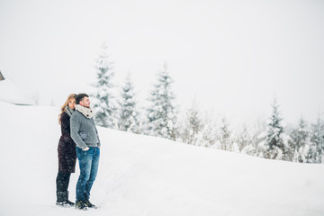 Fototapeta na wymiar Pregnant lady hugs from behind her man posing in snowy forest