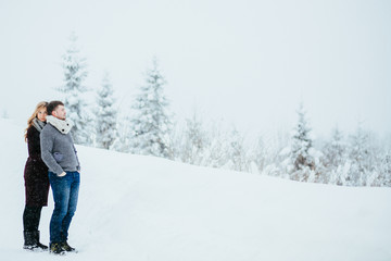 Fototapeta na wymiar Pregnant lady hugs from behind her man posing in snowy forest