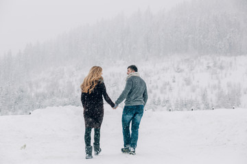 Man and pregnant woman walk to mountains covered with snow