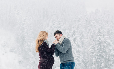 Obraz premium Man holds woman's hands before his mouth while they stand befoe snowy forest