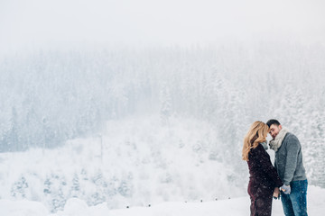 Warm hugs of expacting couple standing before snowy forest