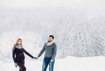 Man in grey sweater and lady in red dress pose before snowy forest