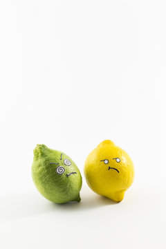 A fresh green and a yellow lemon with sour cartoon style faces on white background