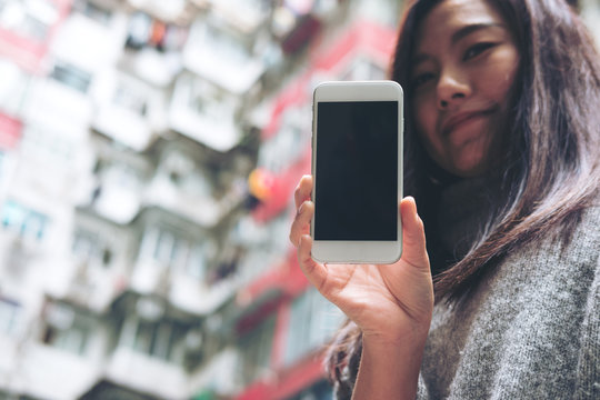 Mockup image of hands holding and showing white mobile phone with blank black screen with a crowded residential building in community in Quarry Bay, Hong Kong background 