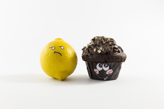Ein frischer, süsser Muffin aus Schokolade und eine gelbe Zitrone mit Gesichtern im Comic Stil vor weissem Hintergrund