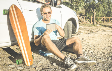 Young hipster fashion guy working remote on computer tablet sitting at car on road trip - New trend...