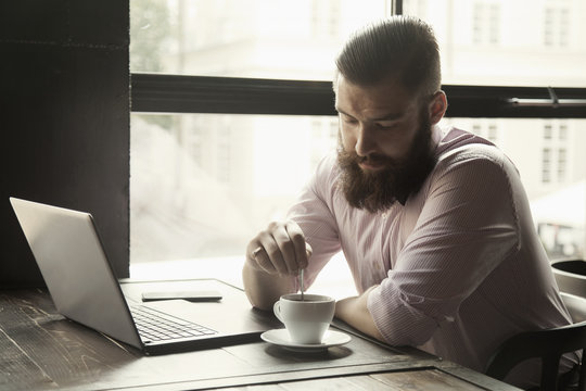 Portrait of a young bearded businessman working with laptop (Success, knowledge, victory, money)