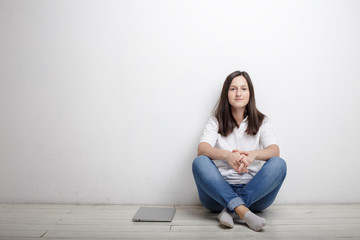 beautiful woman finished work contentedly sitting against the wall on the floor is closed notebook