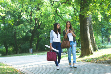 Fototapeta premium Two smiling female students walking in city park.