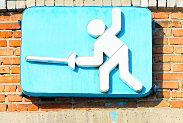 Figurine rapier fencer with a blue background. Red brick wall. Sport fencing.