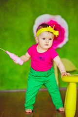 Little girl with toy pin bottle stands before yellow chair