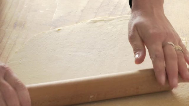 detail of  hands rolling a rolling pin on the fresh dough, making pizza
