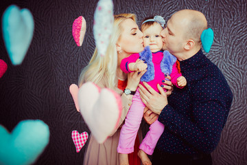 Woman and man in spotted black shirt kiss their little daughter in pink clothes