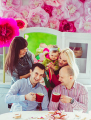 Blonde lady leans with little girl to two men drinking coffee at round table