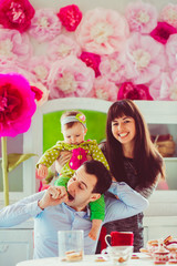 Brunette woman puts little girl in green clothes on man's neck