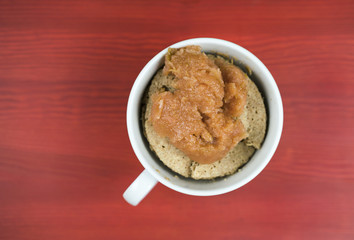 Cake with applesauce inside white cup with handle, shot from above over red wooden surface background