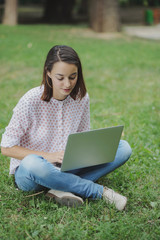 Young woman with laptop sitting on green grass