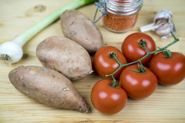 Fresh vegetable ingredients for cooking with vine tomatoes and unpeeled sweet potatoes on a wooden table with onion, red lentils and garlic