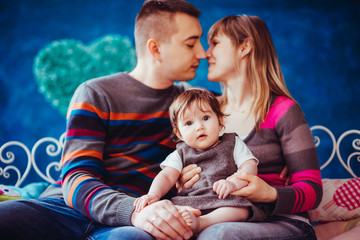 Mom and dad kiss holding their little daughter in grey dress