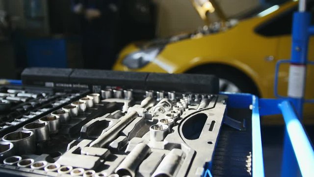 Mechanic repairs yellow car in professional auto service, de-focused time-lapse