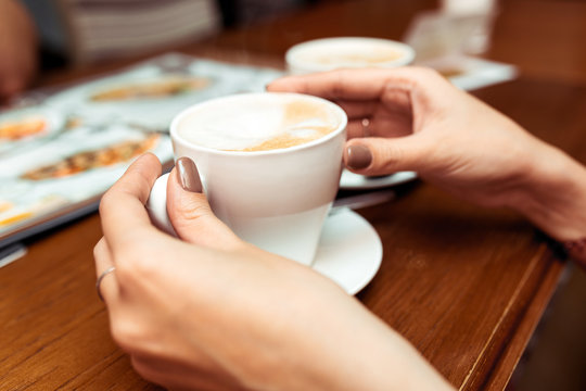 Woman hands holding a cup of coffee with foam over wooden table in cafe