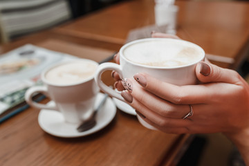 Woman hands holding a cup of coffee with foam over wooden table in cafe
