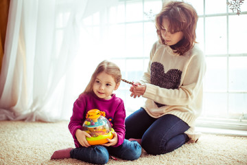 Woman braids girls hair while they play on soft carpet