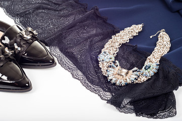 Fototapeta premium Feminine classic fashion concept. Black patent leather shoes with lace dress, perfume and jewelry on white background. Top view