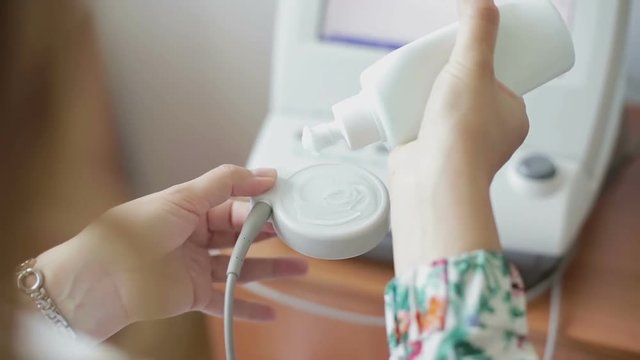 Pregnant woman puts the gel on the sensor for monitoring the heart rate of a baby in the belly.